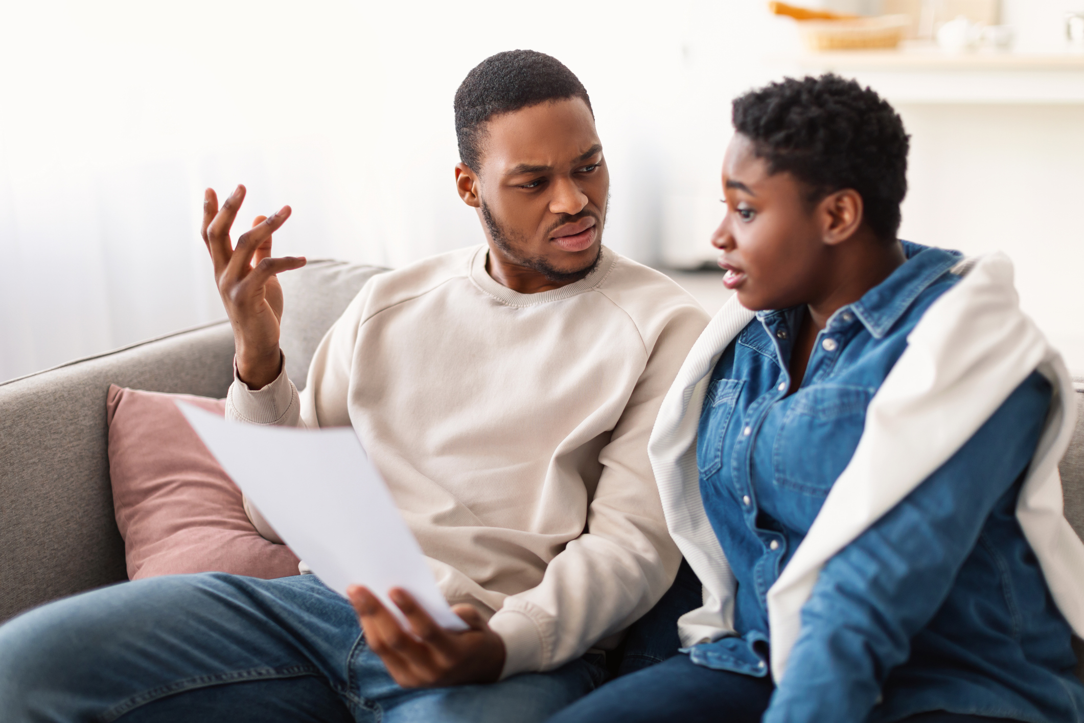 Confused afro couple reading documentation at home, sitting on sofa